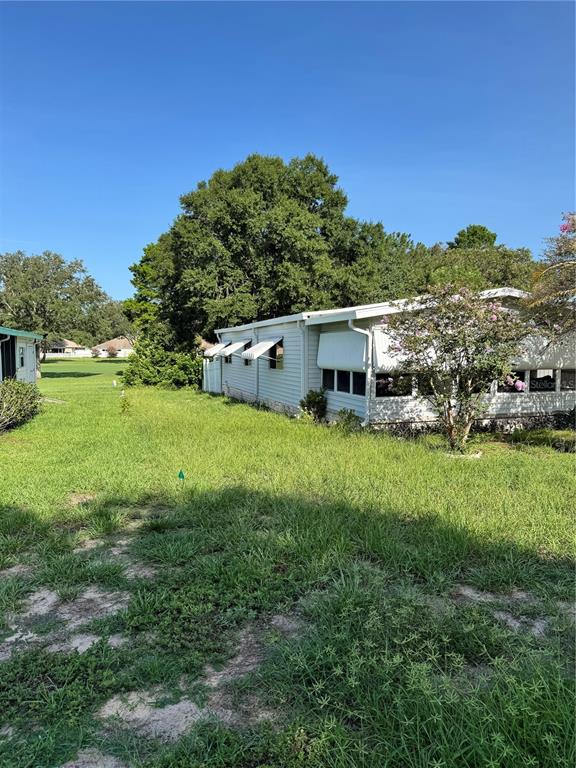 A light-colored mobile home sits on a grassy lot under a clear blue sky — 14251 RIALTO AVENUE, BROOKSVILLE, FL