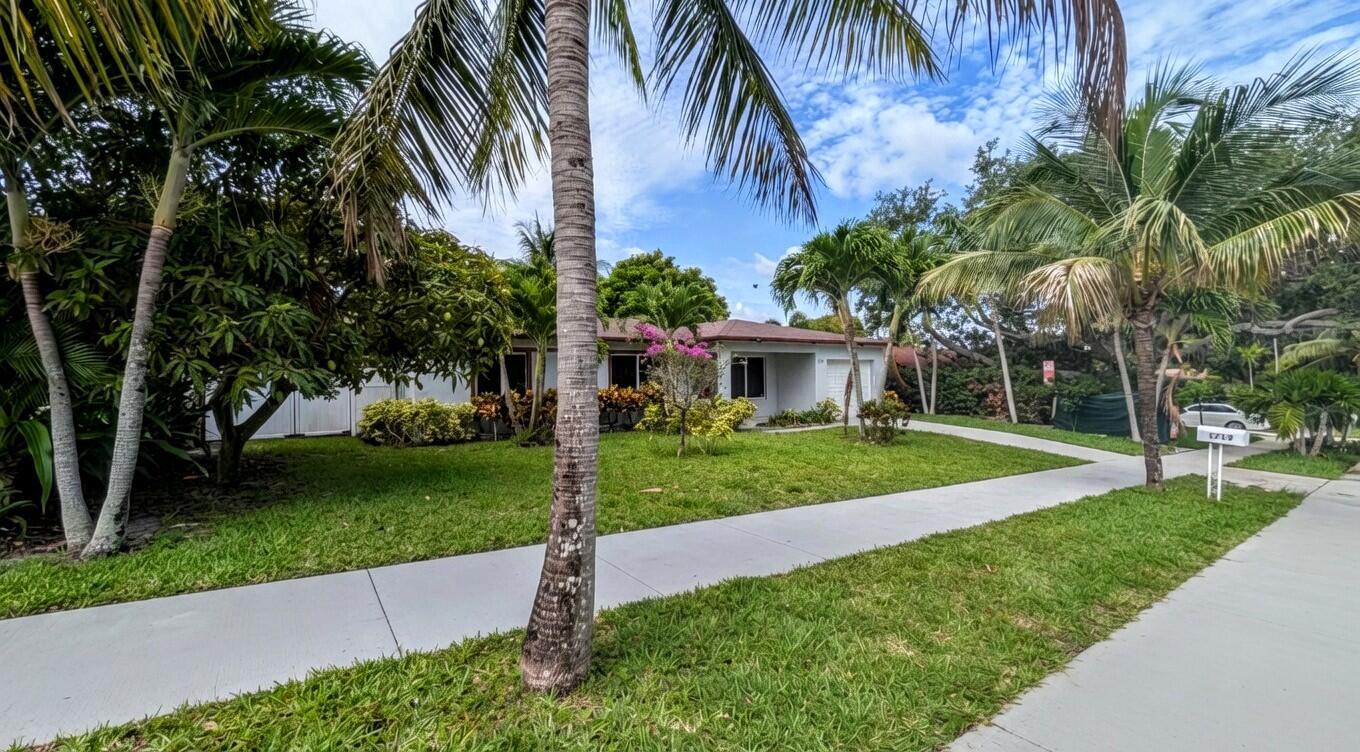 A single-story house with a lawn, palm trees, and a sidewalk in the foreground — 1719 15th Avenue N, FL 33460, FL