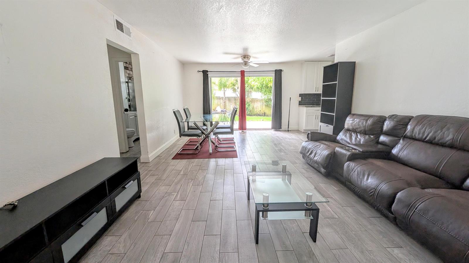 A living and dining area features wood-look tile flooring, a leather sofa, and sliding doors — 1719 15th Avenue N, FL 33460, FL