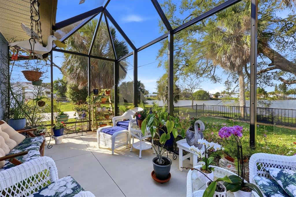 A screened-in patio with white wicker furniture overlooks a lake and palm trees — 4452 TORTOISE ROAD, VENICE, FL