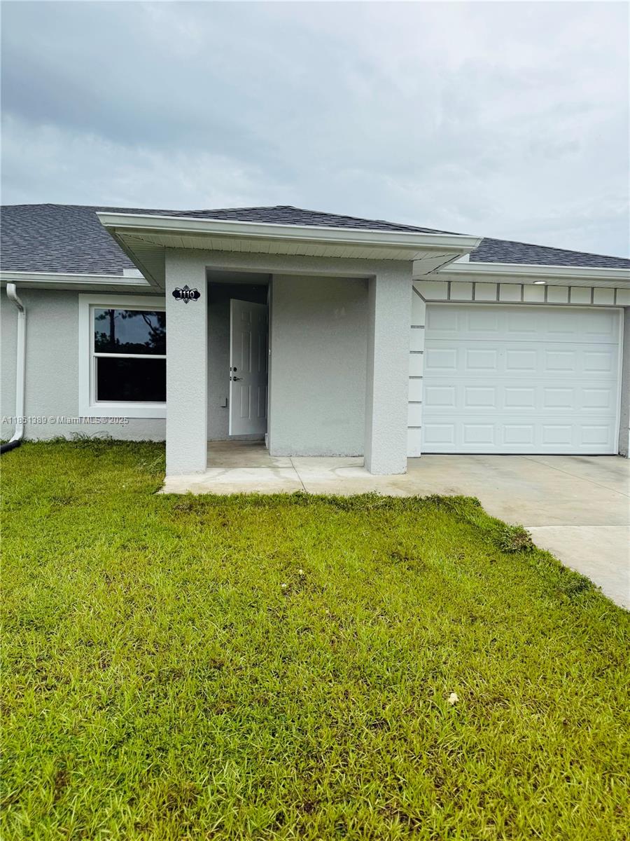 The exterior of a single-story house features a gray stucco facade, a garage, and a porch — 1110 Augusta St E # 1110, Lehigh Acres FL 33974, LEHIGH ACRES, FL