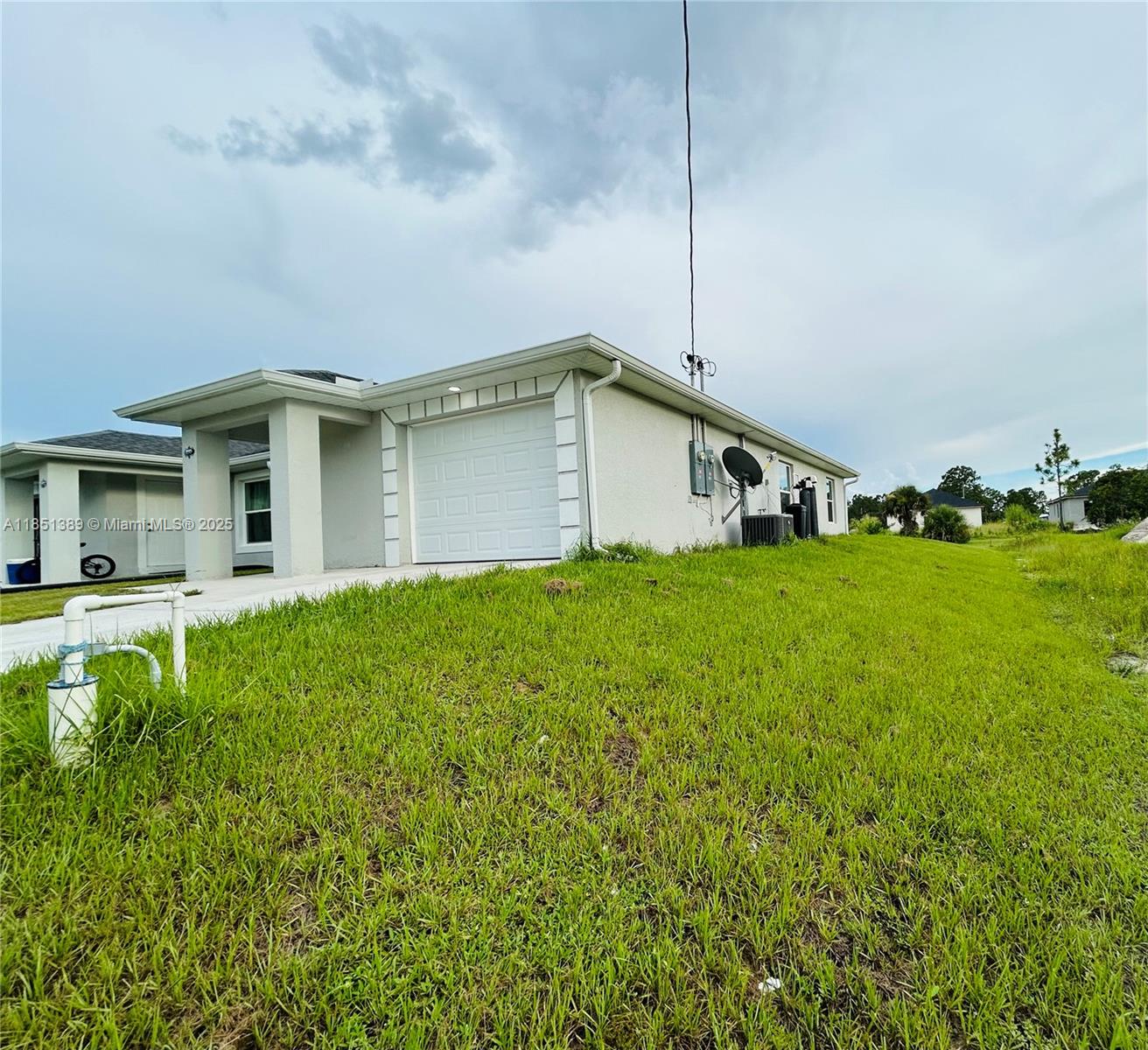A side view of a light-colored house with a garage and a grassy yard — 1110 Augusta St E # 1110, Lehigh Acres FL 33974, LEHIGH ACRES, FL