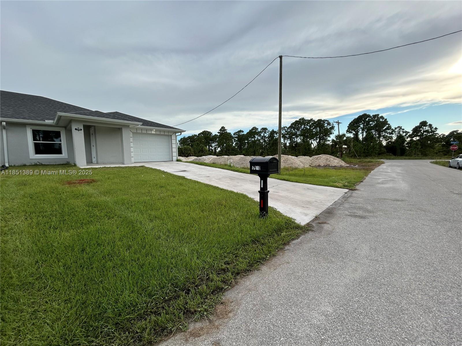 A single-story house with a white garage and a mailbox sits beside a paved road — 1110 Augusta St E # 1110, Lehigh Acres FL 33974, LEHIGH ACRES, FL