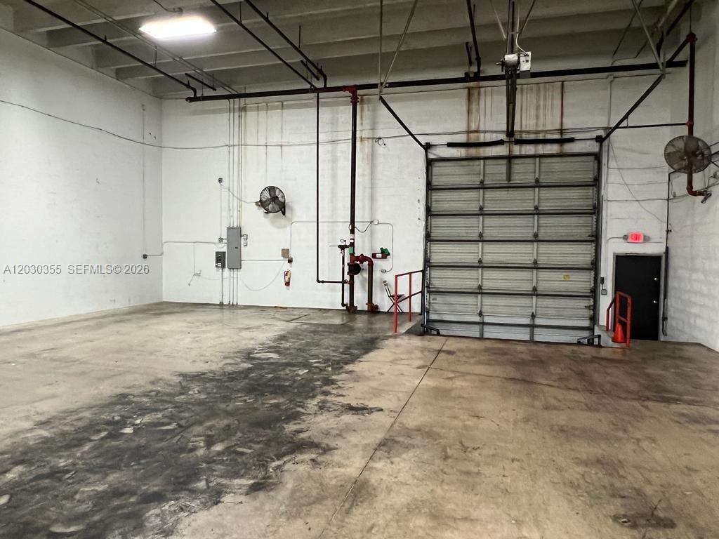 An industrial warehouse space features a concrete floor, a roll-up door, and exposed piping — 2281 NW 95th Ave, Doral FL 33172, DORAL, FL