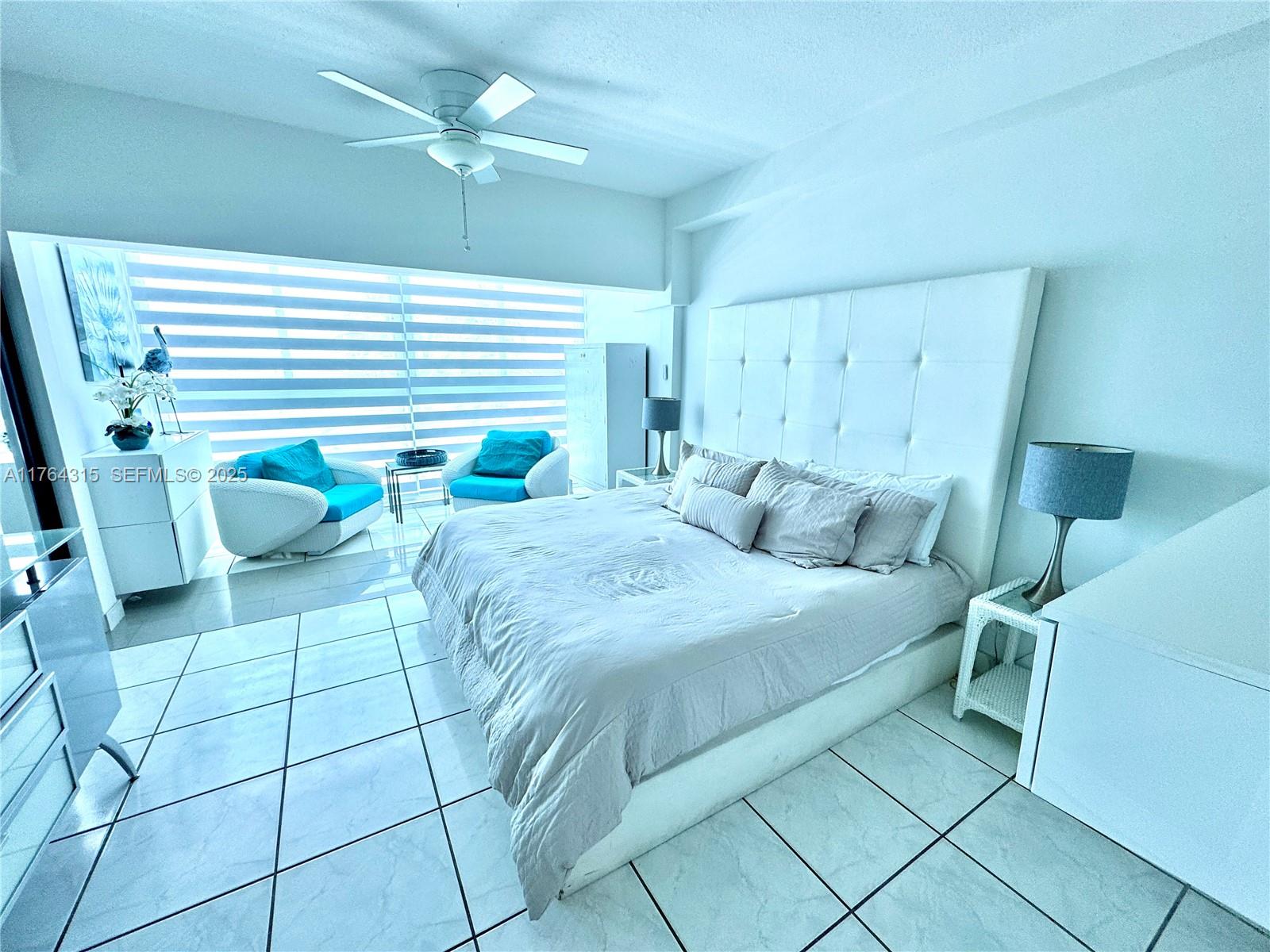 A bright bedroom features a large white tufted headboard, tiled floors, and two blue chairs — 5445 Collins Ave # 11, Miami Beach FL 33140, MIAMI BEACH, FL