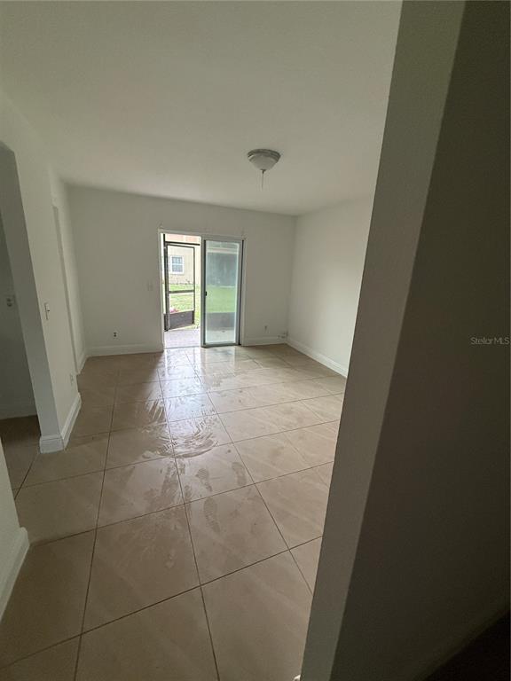 A room with light-colored tile flooring and a sliding glass door leading to a patio — 9800 TURF WAY UNIT 1, ORLANDO, FL