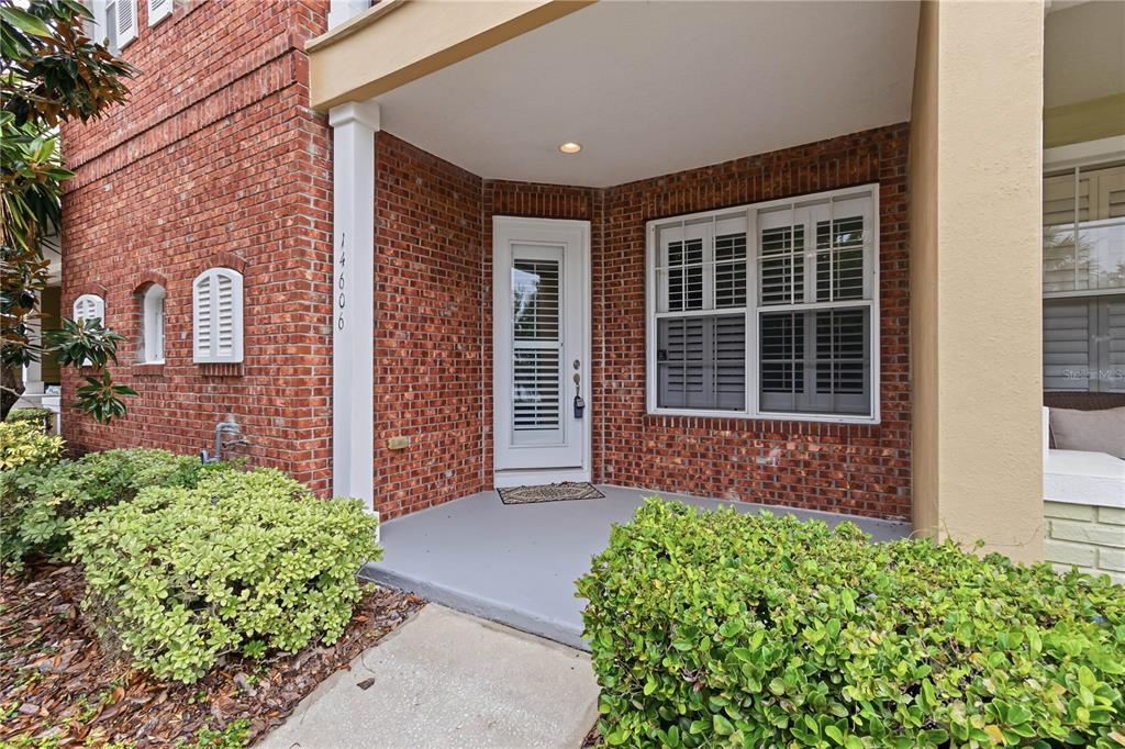 A brick exterior home features a covered front porch, a white door, and green landscaping — 14606 BOURNEMOUTH ROAD, TAMPA, FL