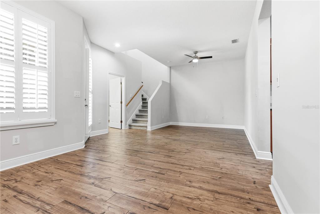 An empty room features wood-look flooring, white walls, a ceiling fan, and a staircase — 14606 BOURNEMOUTH ROAD, TAMPA, FL