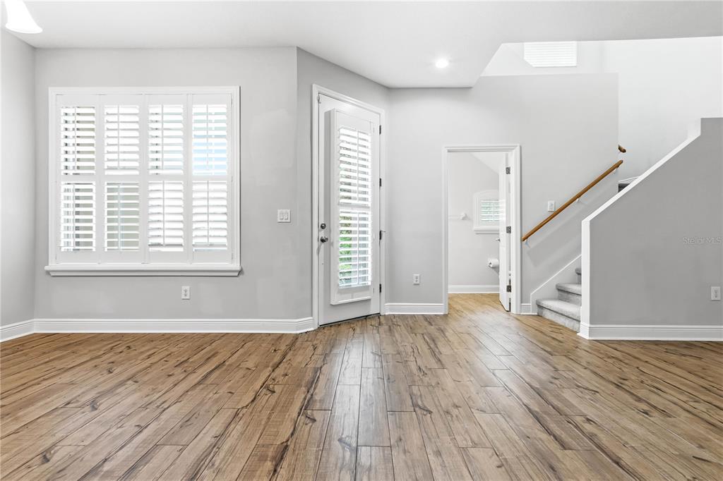A bright room with light gray walls, wood-look flooring, plantation shutters, and a staircase — 14606 BOURNEMOUTH ROAD, TAMPA, FL