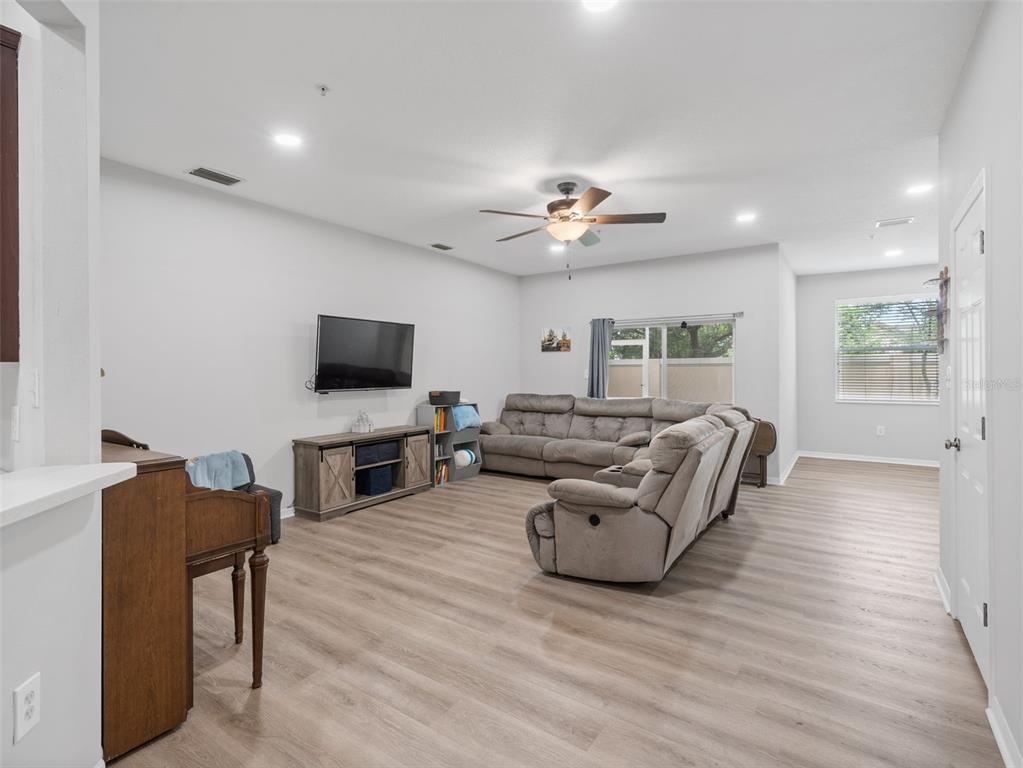A living room features light wood-look flooring, a gray sectional sofa, and a wall-mounted television — 3831 PARKRIDGE CIRCLE UNIT 1-104, SARASOTA, FL