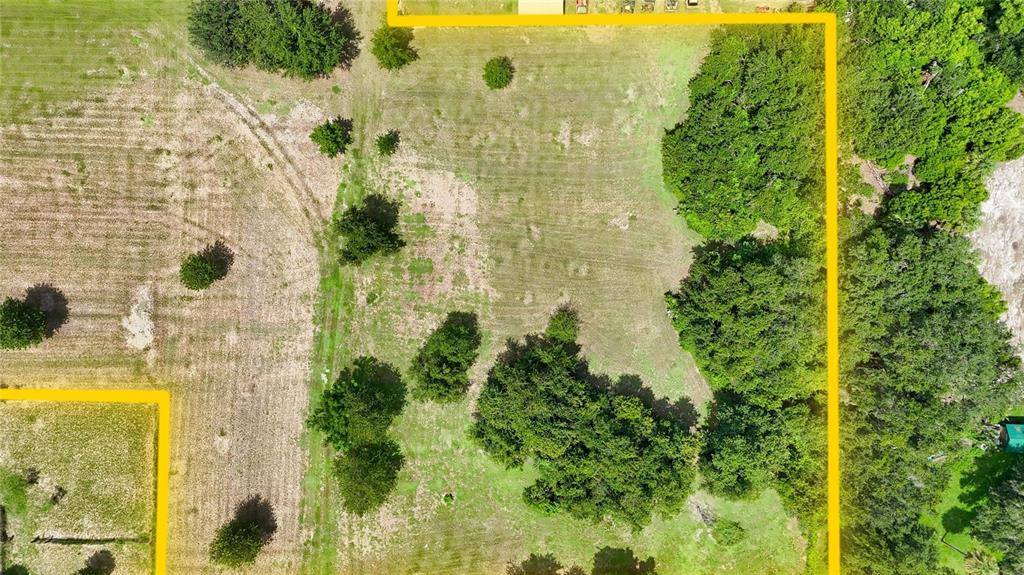 An aerial view shows a grassy, tree-lined plot of land outlined in yellow — 2452 WELCOME ROAD, LITHIA, FL
