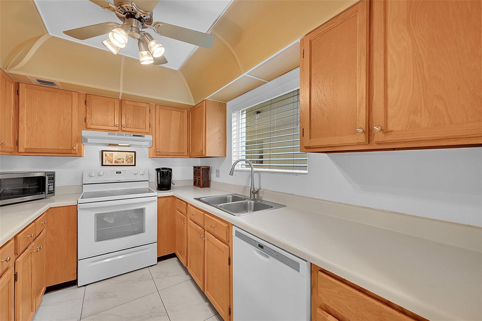 A kitchen with light wood cabinets, white appliances, a double sink, and a tray ceiling — 111 Deer Creek Boulevard # 108, Deerfield Beach FL 33442, DEERFIELD BEACH, FL