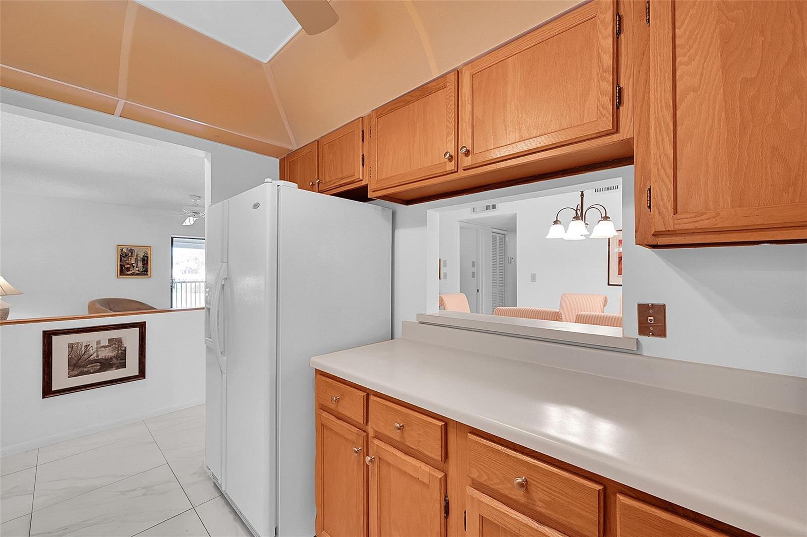 A kitchen features light wood cabinets, white countertops, a white refrigerator, and a pass-through window — 111 Deer Creek Boulevard # 108, Deerfield Beach FL 33442, DEERFIELD BEACH, FL
