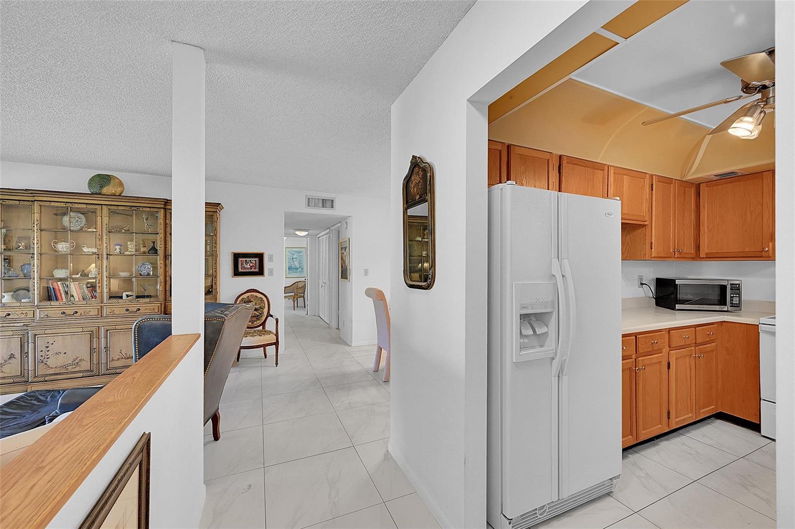A white refrigerator stands in a kitchen with oak cabinets next to a dining area — 111 Deer Creek Boulevard # 108, Deerfield Beach FL 33442, DEERFIELD BEACH, FL