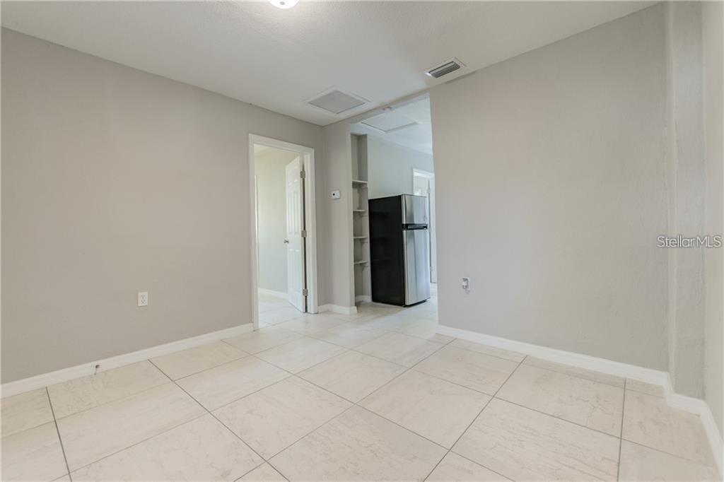 A room with light-colored tile flooring leads to a kitchen area with a refrigerator — 5106 W RICHARDSON AVENUE UNIT B, TAMPA, FL