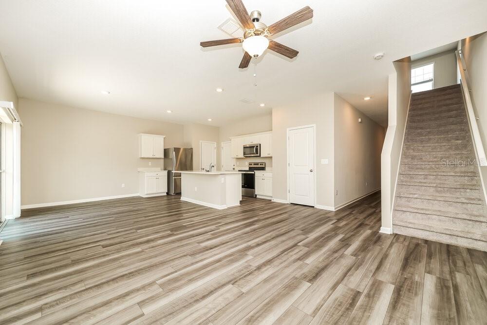 An open-concept kitchen and living area features wood-look flooring, white cabinetry, and a carpeted staircase — 2052 HARRIS HAWK AVENUE, RUSKIN, FL