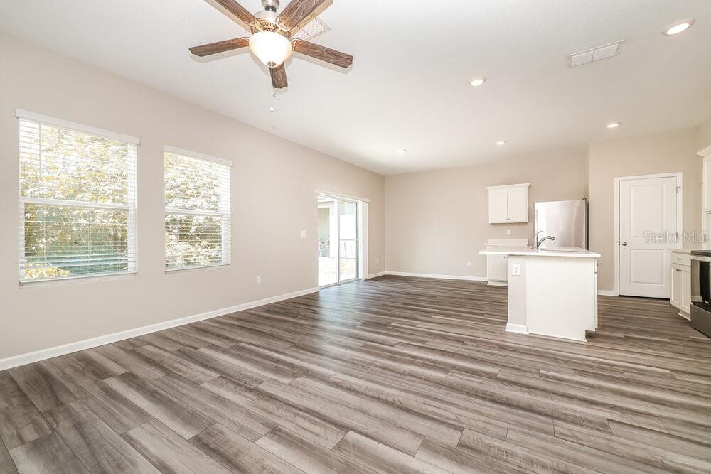 An open-concept living area features light-colored walls, wood-look flooring, a ceiling fan, and kitchen — 2052 HARRIS HAWK AVENUE, RUSKIN, FL