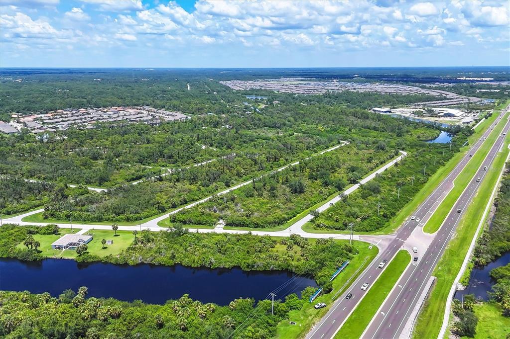 An aerial view shows a large, wooded lot bordered by a canal and a highway — 1553  & 1561 FRISCO TERRACE, PORT CHARLOTTE, FL