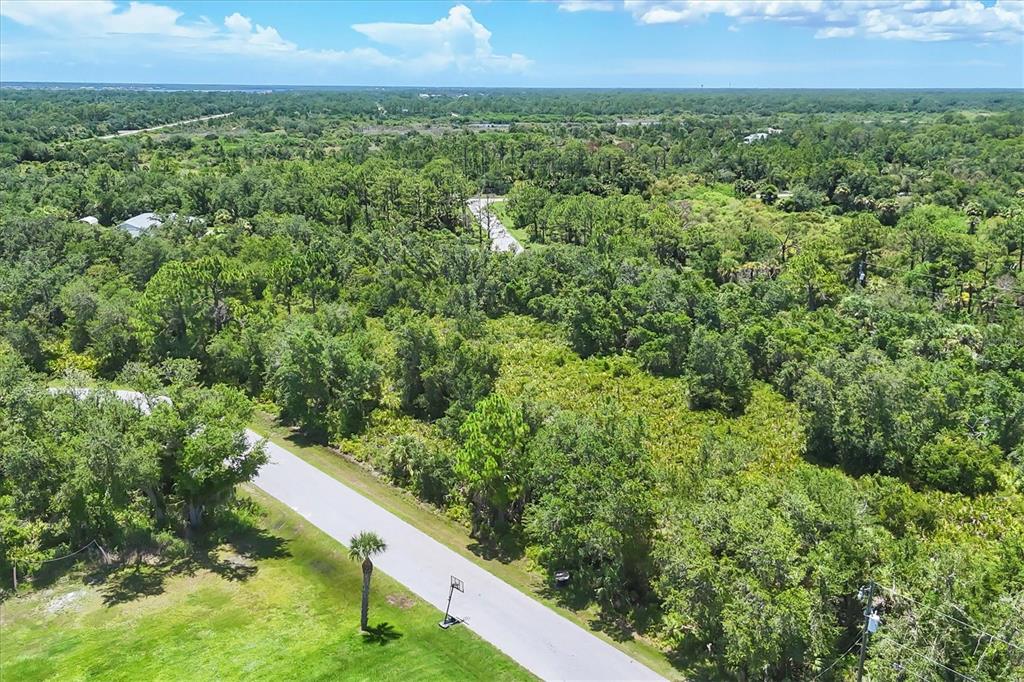 An aerial view shows a paved road winding through a dense, wooded residential area — 1553  & 1561 FRISCO TERRACE, PORT CHARLOTTE, FL
