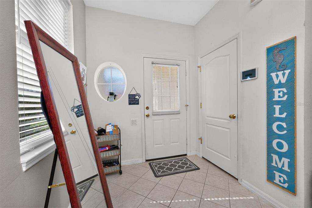An entryway features tiled floors, a full-length mirror, a white door, and a welcome sign — 1158 JONAH DR, NORTH PORT, FL