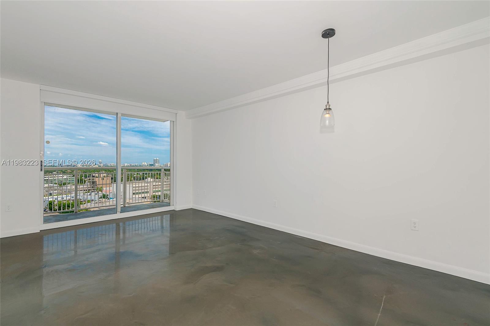 An empty room features polished concrete floors, white walls, and a sliding glass balcony door — 1688 West Ave # 07, Miami Beach FL 33139, MIAMI BEACH, FL