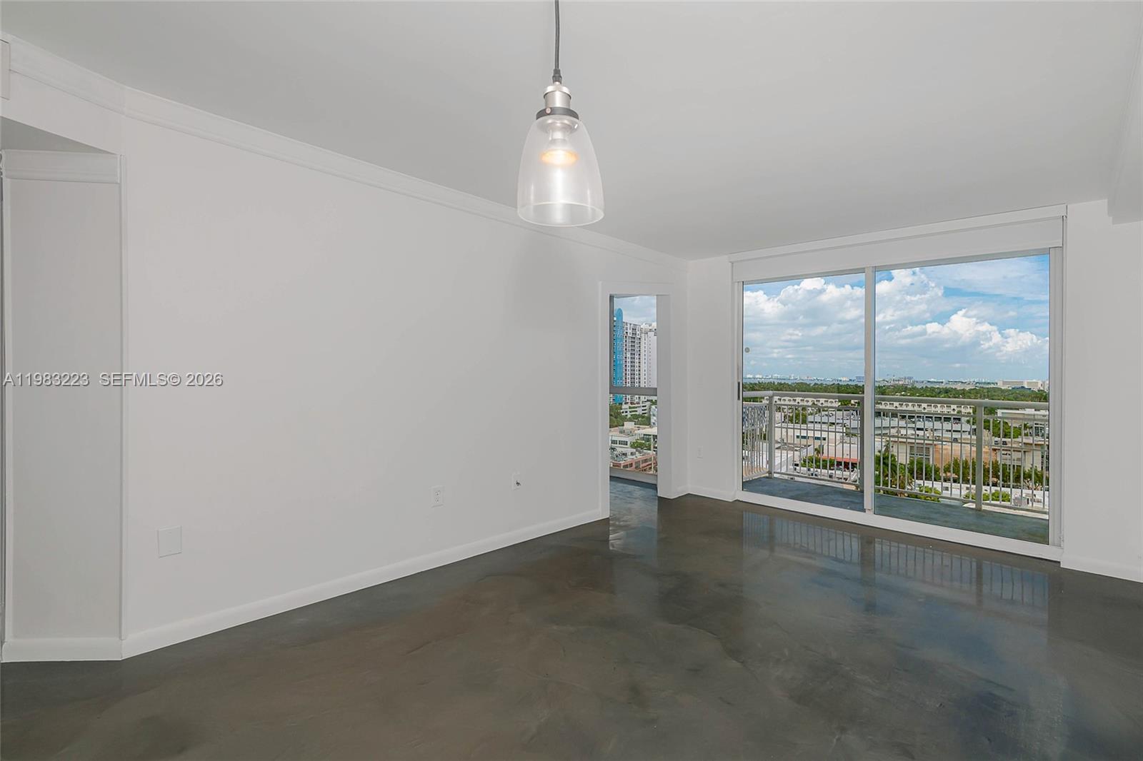 An empty room features polished concrete floors, a single pendant light, and a balcony view — 1688 West Ave # 07, Miami Beach FL 33139, MIAMI BEACH, FL
