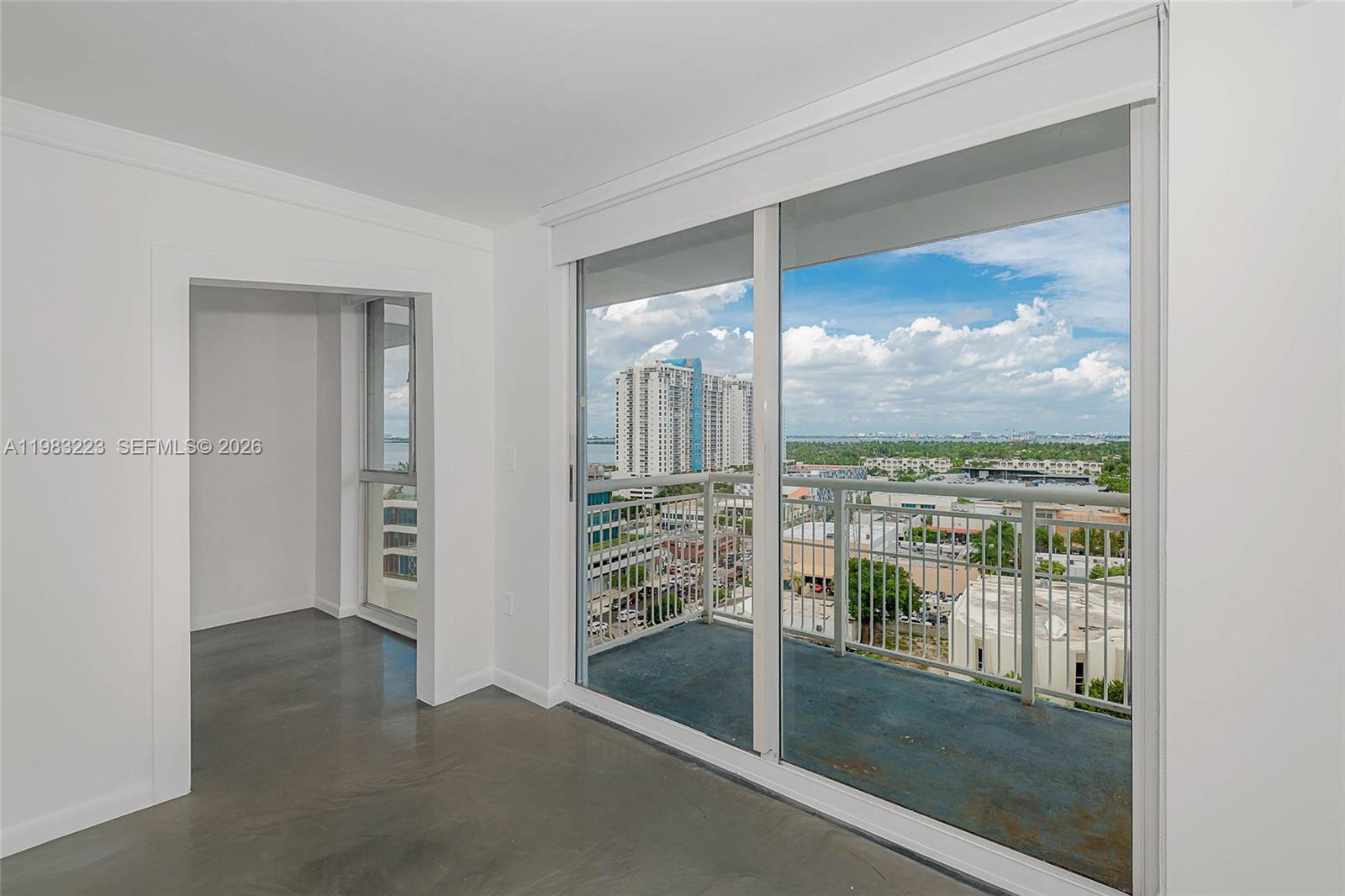An empty room with gray concrete floors features a balcony and floor-to-ceiling sliding glass doors — 1688 West Ave # 07, Miami Beach FL 33139, MIAMI BEACH, FL
