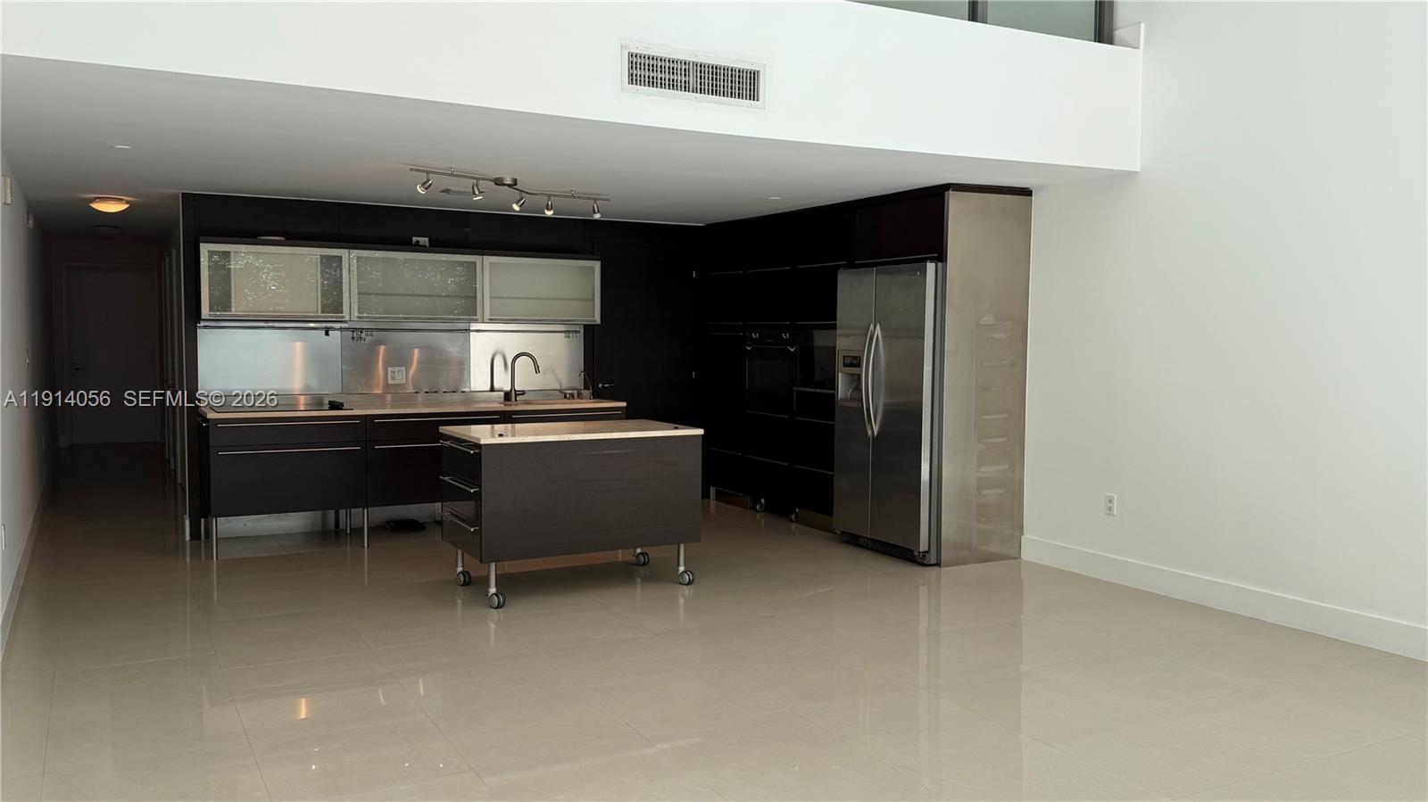A modern kitchen features dark cabinetry, stainless steel appliances, and a movable center island — 6000 Collins Ave # 305, Miami Beach FL 33140, MIAMI BEACH, FL
