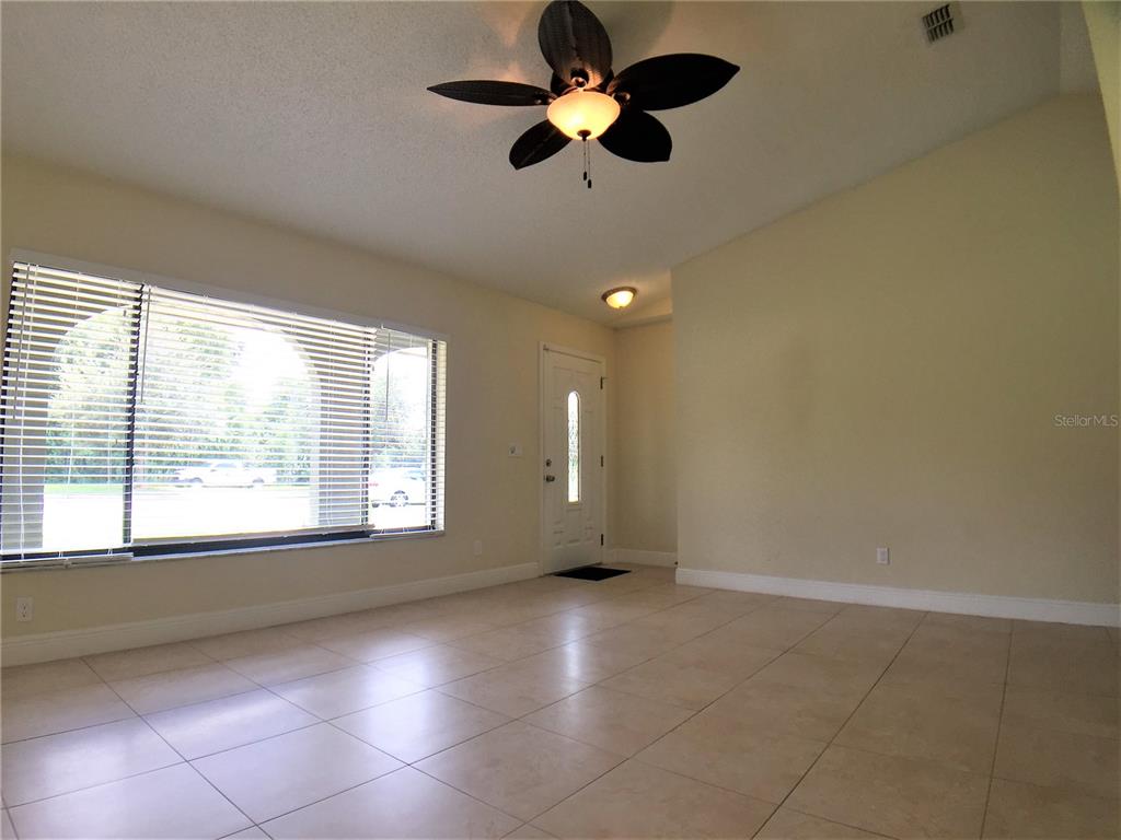 A bright living room features light tile flooring, a ceiling fan, and a front door — 1927 E LAKE DRIVE, CASSELBERRY, FL