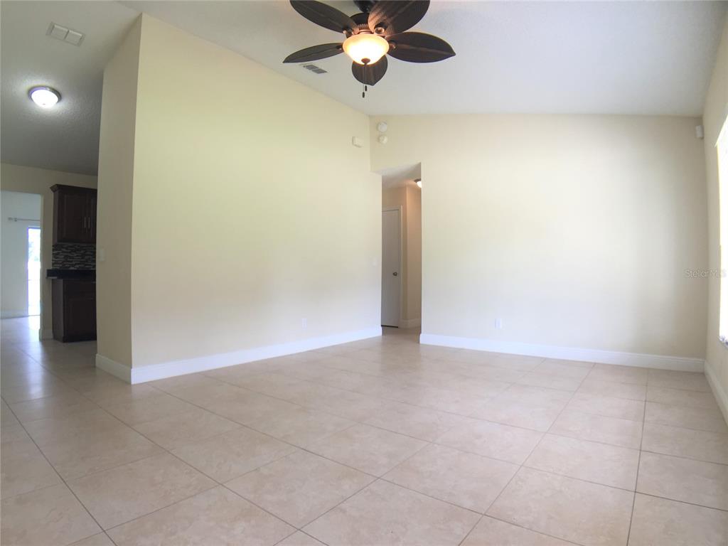 An empty living room with beige tile floors, light walls, and a ceiling fan — 1927 E LAKE DRIVE, CASSELBERRY, FL