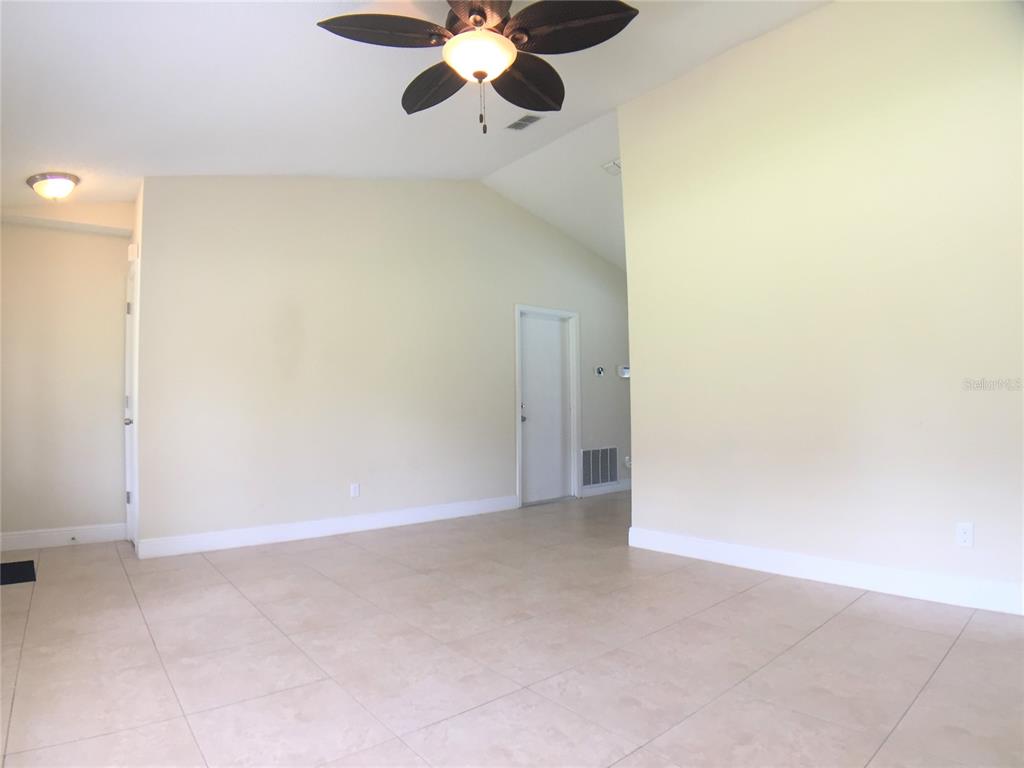 An empty room features light-colored tile flooring, beige walls, a vaulted ceiling, and a ceiling fan — 1927 E LAKE DRIVE, CASSELBERRY, FL
