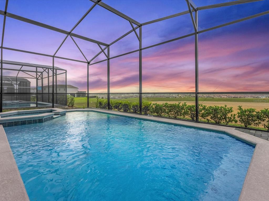 A swimming pool and spa are enclosed by a screened lanai overlooking a grassy field — 1891 SUMMER DRIVE, DAVENPORT, FL