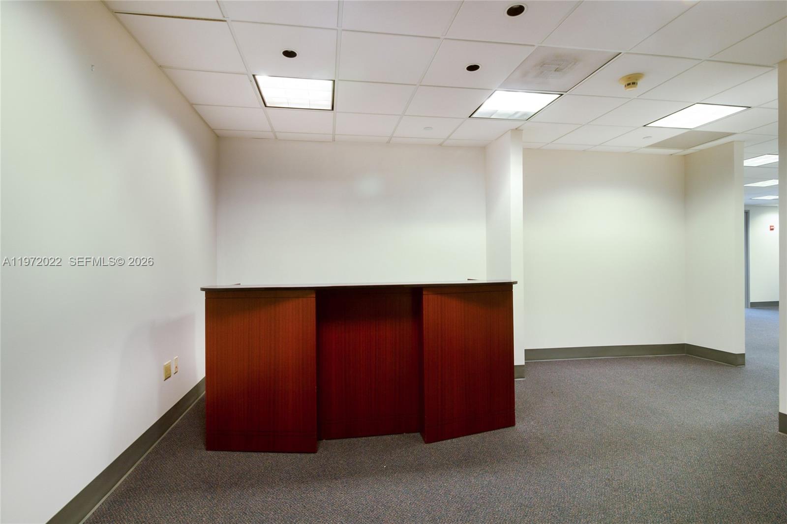 An empty office space features a wooden reception desk, white walls, and gray carpeting — 1200 Brickell Ave # B, Miami FL 33131, MIAMI, FL