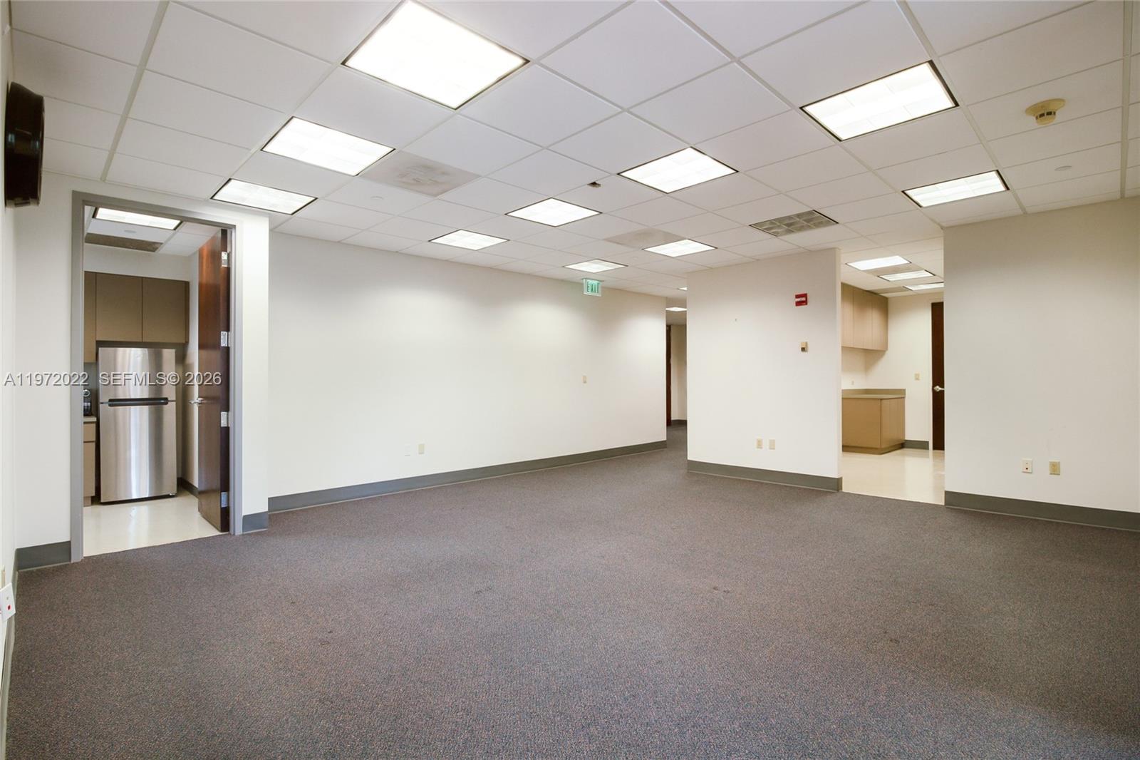 An empty office space features gray carpeting, white walls, drop ceilings, and two small kitchenettes — 1200 Brickell Ave # B, Miami FL 33131, MIAMI, FL
