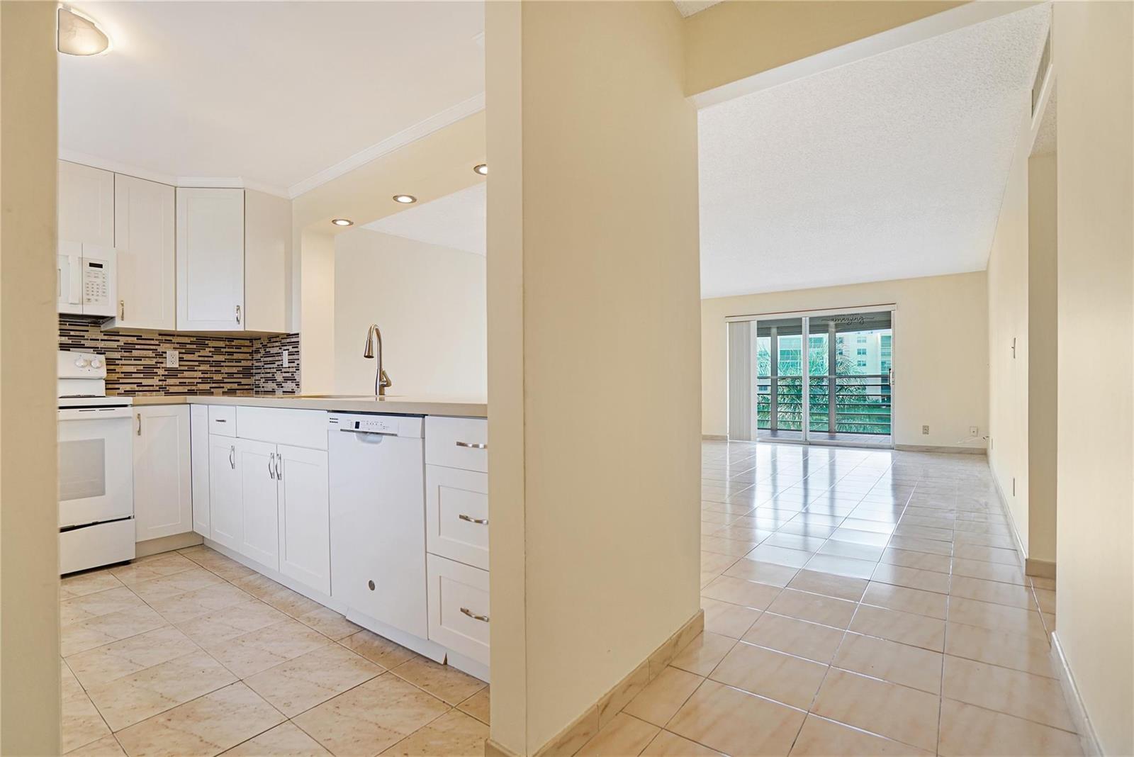 A kitchen with white cabinets and tile flooring opens into a bright living area — 111 SE 3rd Avenue # 306, Dania Beach FL 33004, DANIA BEACH, FL