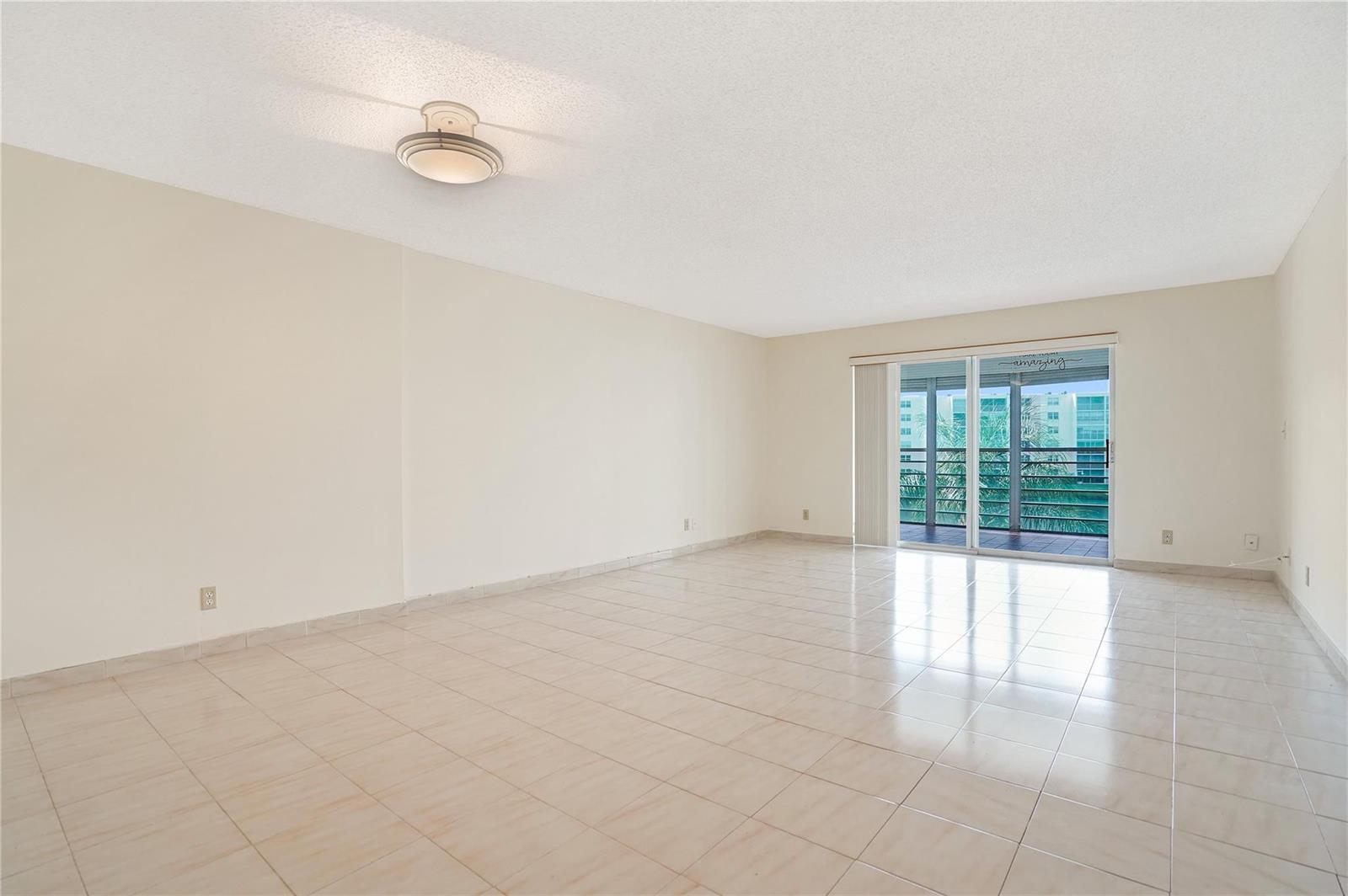 An empty living room features light-colored tile flooring, white walls, and a sliding glass door — 111 SE 3rd Avenue # 306, Dania Beach FL 33004, DANIA BEACH, FL