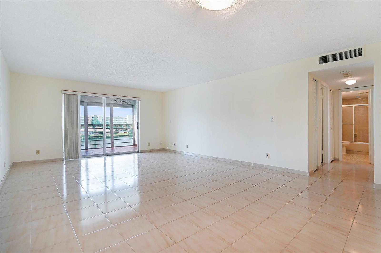 An empty living room with light-colored tile flooring, white walls, and a sliding glass door — 111 SE 3rd Avenue # 306, Dania Beach FL 33004, DANIA BEACH, FL