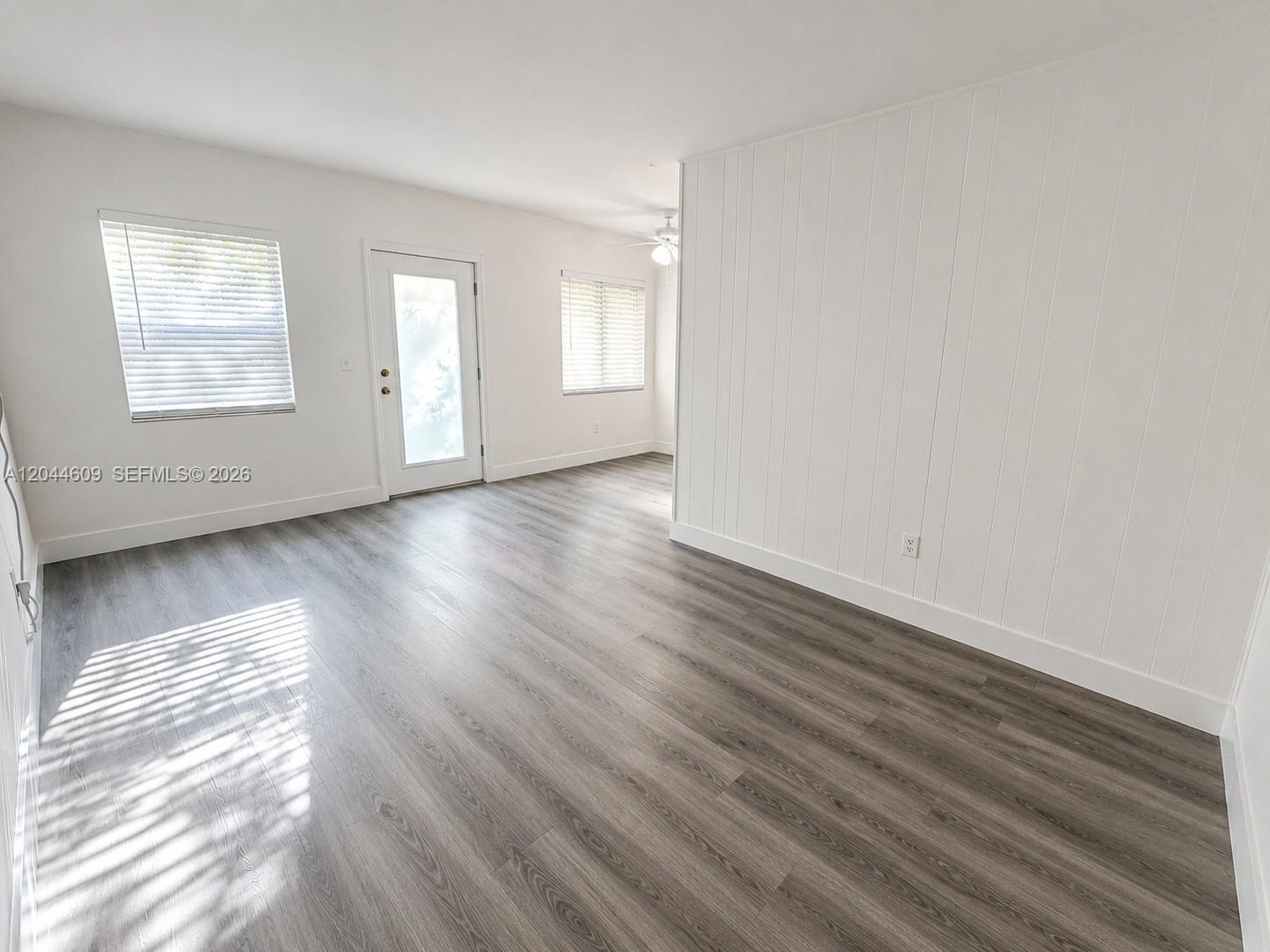 An empty room features white walls, wood-look flooring, a glass-paneled door, and two windows — 34 Madeira Ave # 3, Coral Gables FL 33134, CORAL GABLES, FL
