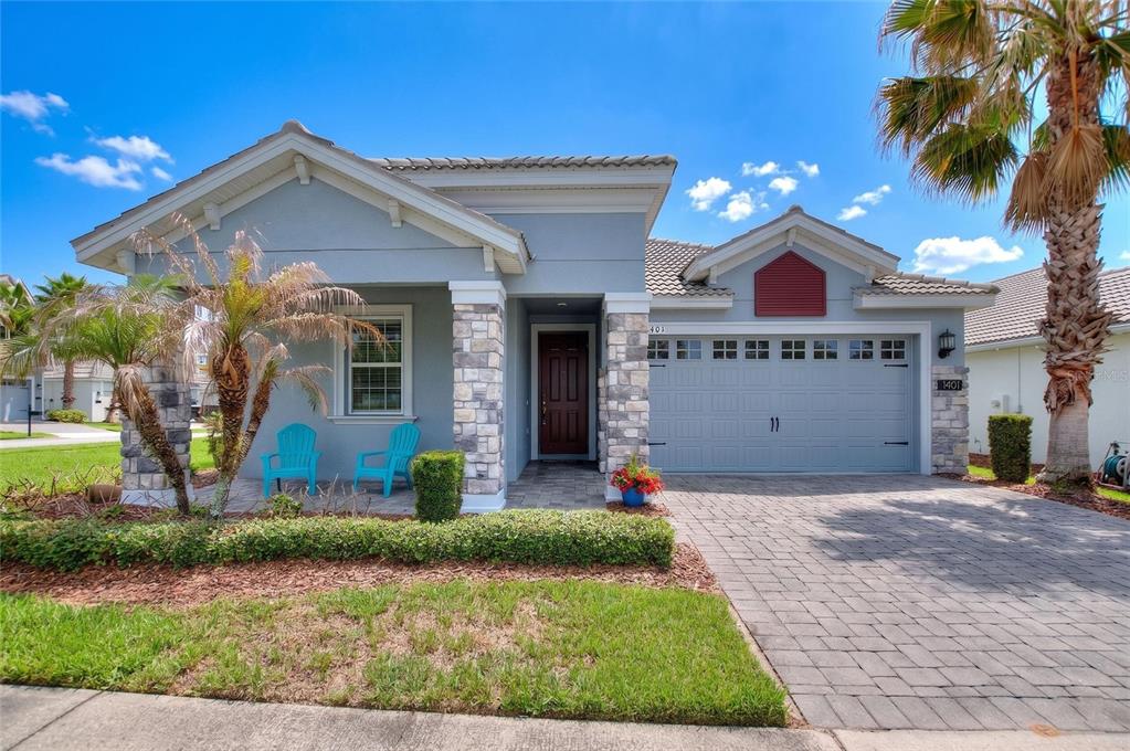 A light blue single-story house features a stone-accented porch, a two-car garage, and landscaping — 1401 CLUBMAN DRIVE, DAVENPORT, FL