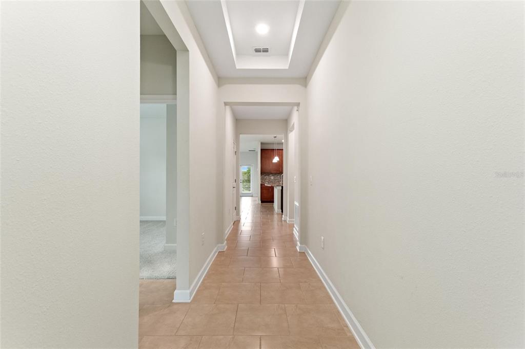A long hallway with tile flooring leads toward a kitchen and a glass exterior door — 1401 CLUBMAN DRIVE, DAVENPORT, FL