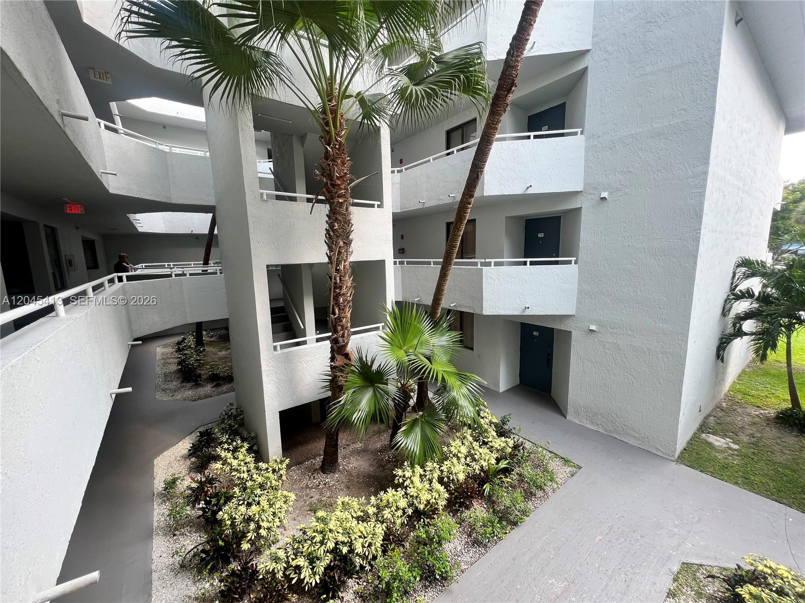 An outdoor courtyard features a central palm tree surrounded by landscaping and multi-story building balconies — 8255 SW 152nd Ave # 209, Miami FL 33193, MIAMI, FL
