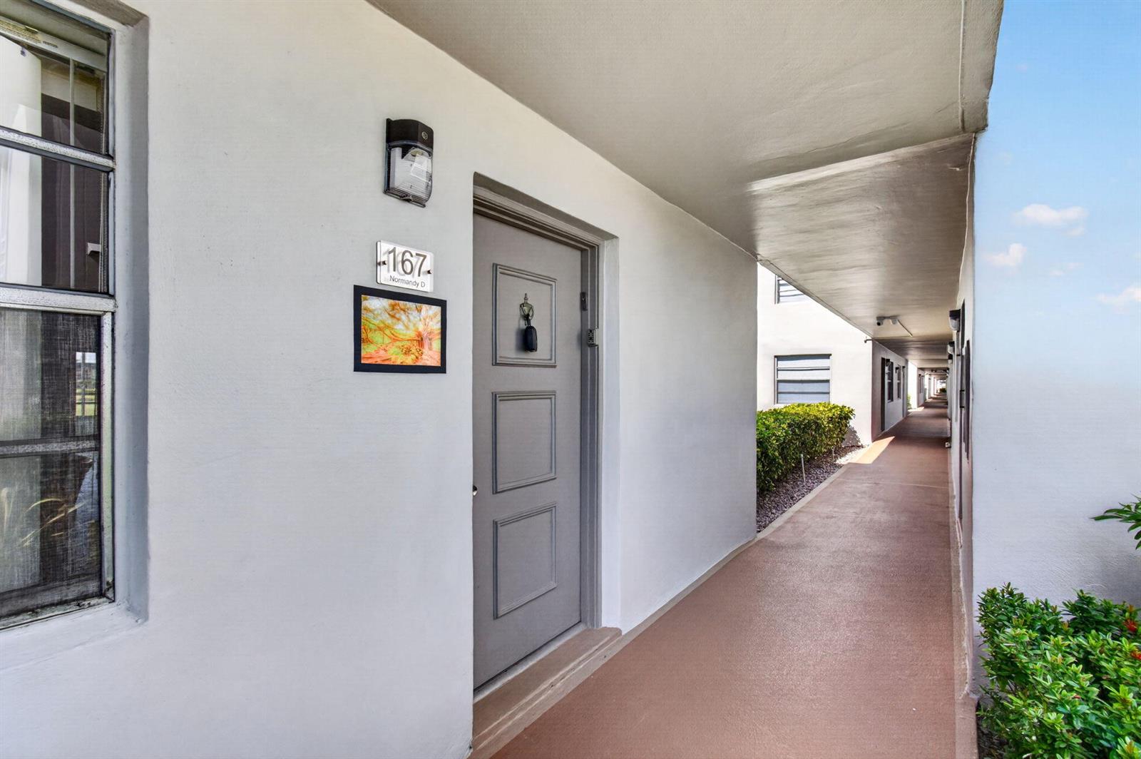 An exterior view of an apartment entrance with a gray door and a numbered sign — 167 Normandy # D, Delray Beach FL 33484, DELRAY BEACH, FL