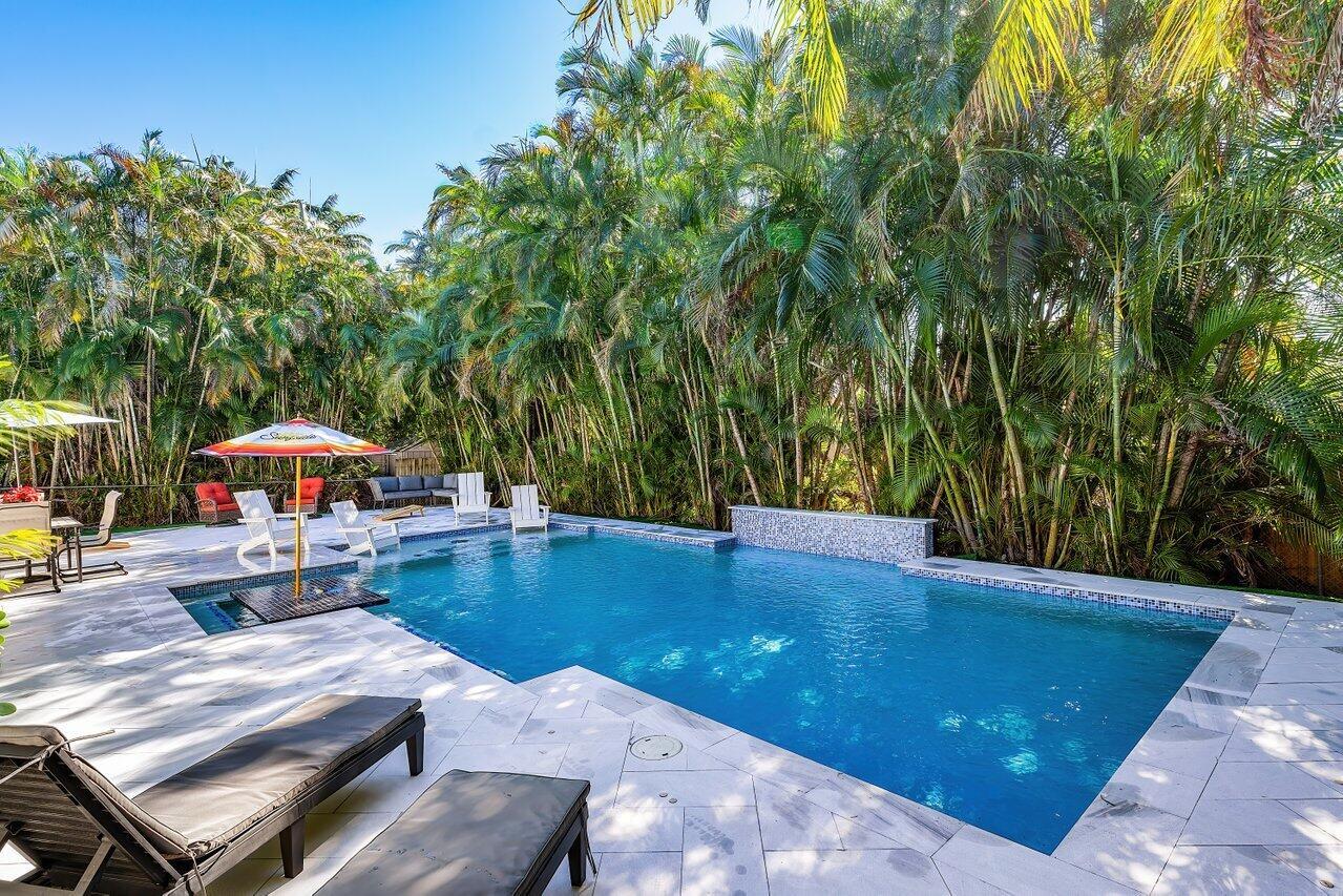 A rectangular swimming pool with a tiled water feature sits on a patio with lounge chairs — 630 NE 15th Place, Boynton Beach FL 33435, BOYNTON BEACH, FL