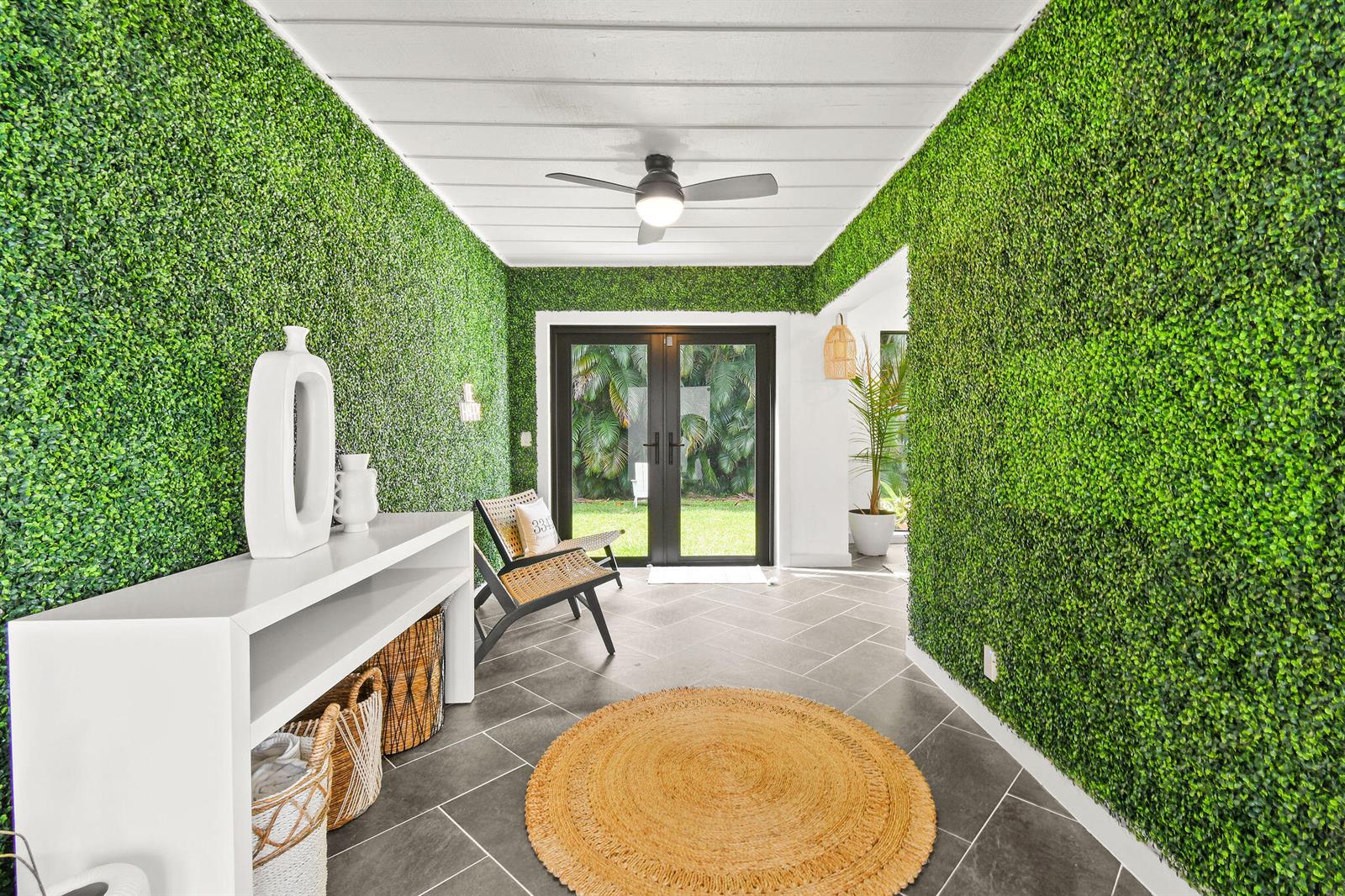 An entryway features artificial boxwood walls, a white console table, and a round jute rug — 630 NE 15th Place, Boynton Beach FL 33435, BOYNTON BEACH, FL