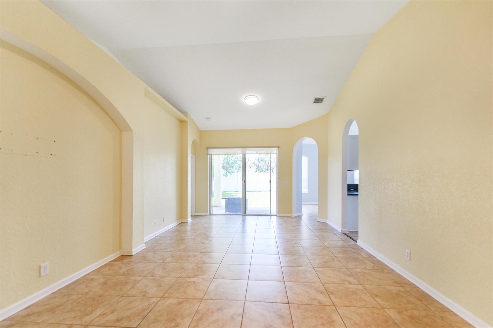 An empty room with beige walls, tile flooring, arched doorways, and sliding glass patio doors — 5544 Spanish River Road, Fort Pierce FL 34951, FORT PIERCE, FL