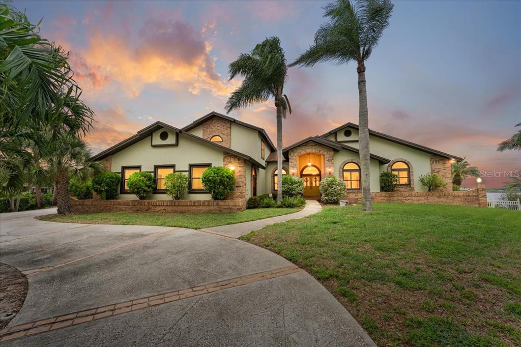 A two-story house with a brick base, stucco walls, and a curved driveway at sunset — 1589 MARY LANE, TARPON SPRINGS, FL