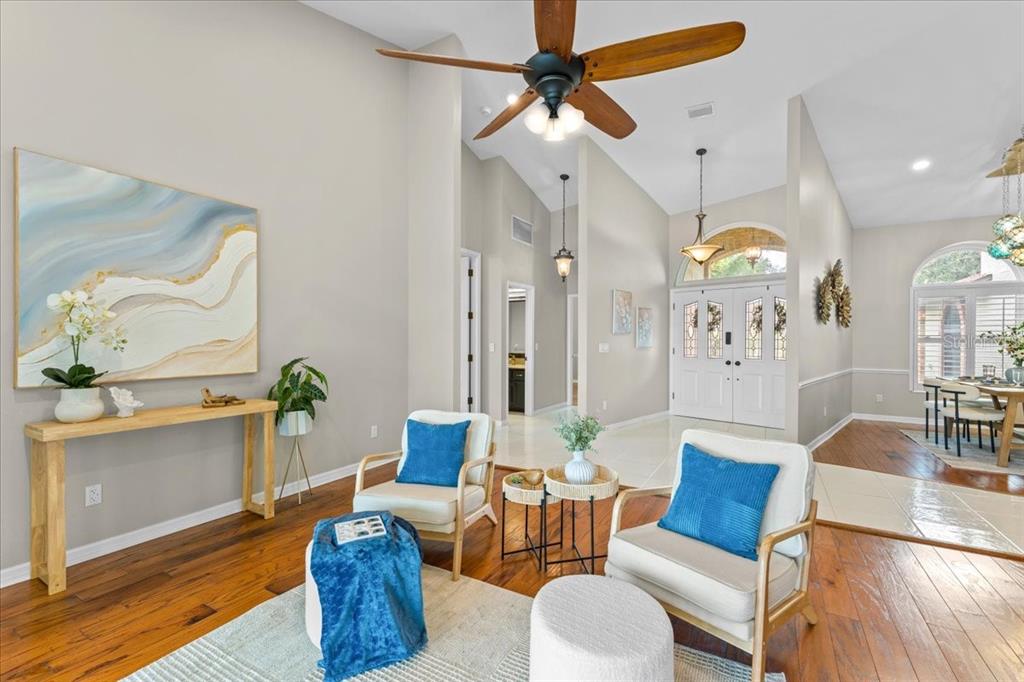 A bright living room features hardwood floors, two armchairs, a console table, and vaulted ceilings — 1589 MARY LANE, TARPON SPRINGS, FL