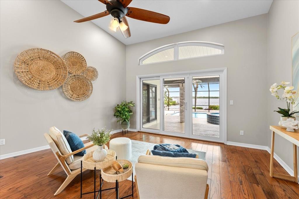 A sunlit living room features hardwood floors, a vaulted ceiling, and sliding doors to a pool — 1589 MARY LANE, TARPON SPRINGS, FL