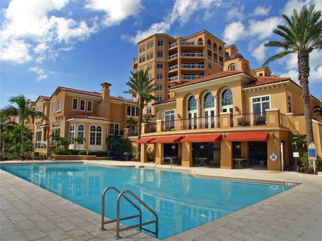 A swimming pool sits in front of a multi-story Mediterranean-style building with red-tiled roofs — 521 MANDALAY AVENUE UNIT 704, CLEARWATER BEACH, FL