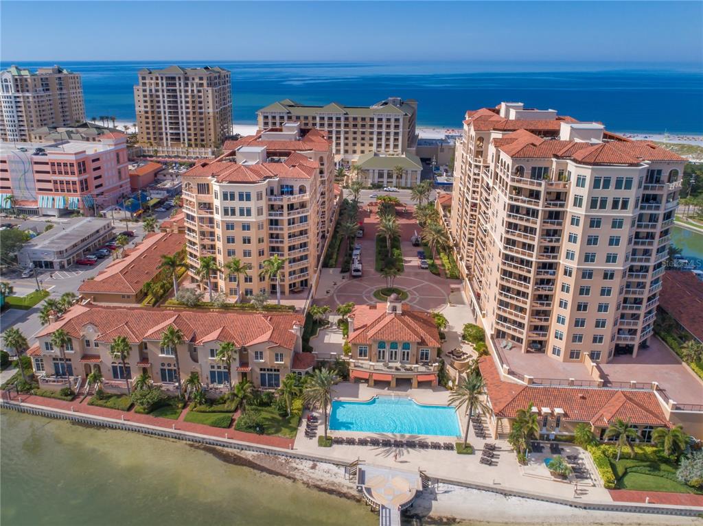 An aerial view of a waterfront resort complex featuring multiple buildings, a pool, and landscaping — 521 MANDALAY AVENUE UNIT 704, CLEARWATER BEACH, FL
